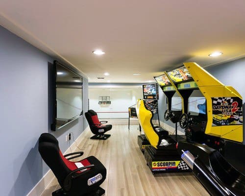 Arcade room with racing simulators, gaming chairs, and large TV screen on a light wood floor