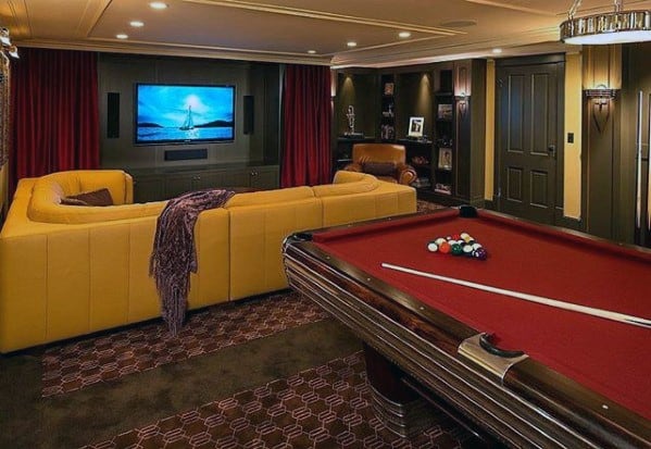 Retro-style man cave with yellow sectional sofa, pool table, and large TV in a cozy entertainment space.