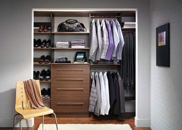 A neatly organized closet with clothes, shelves, a chair, and an electronic device on a wooden cabinet