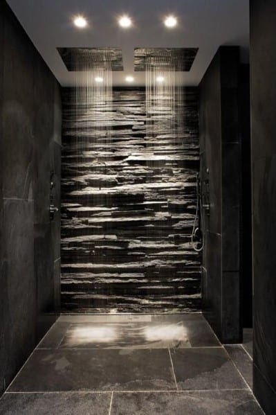 Modern shower with dark stone walls, dual rainfall showerheads, and dramatic lighting.