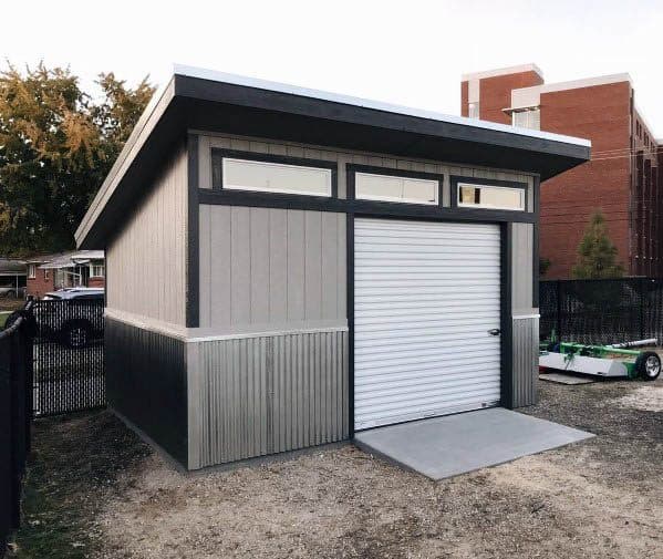 Modern backyard shed with slanted roof and white roll-up garage door.