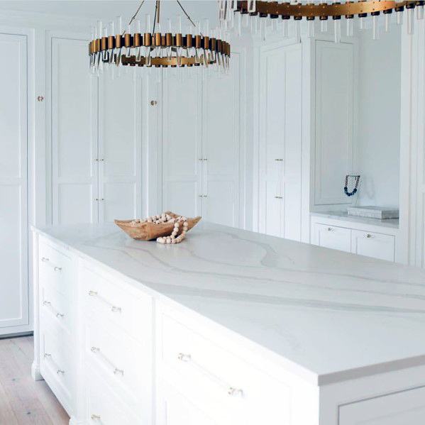 Elegant kitchen featuring round brass chandeliers with tube LEDs above a white marble island, complemented by sleek white cabinetry and minimalist decor.