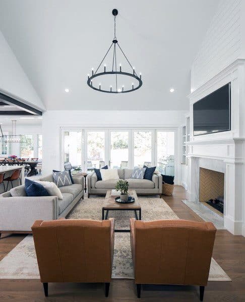 Stylish living room with two tan chairs, gray sofas, a coffee table, large windows, and a black chandelier