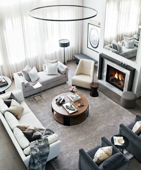 Modern living room with gray sofas, armchairs, a wooden coffee table, and a lit fireplace featuring a neutral color scheme