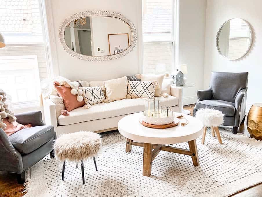 Cozy living room with a sofa, pillows, two chairs, round mirrors, a rug, and a round coffee table with decor