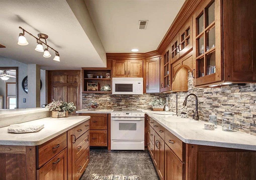 Rustic kitchen with wood cabinets, stone backsplash, and neutral countertops.