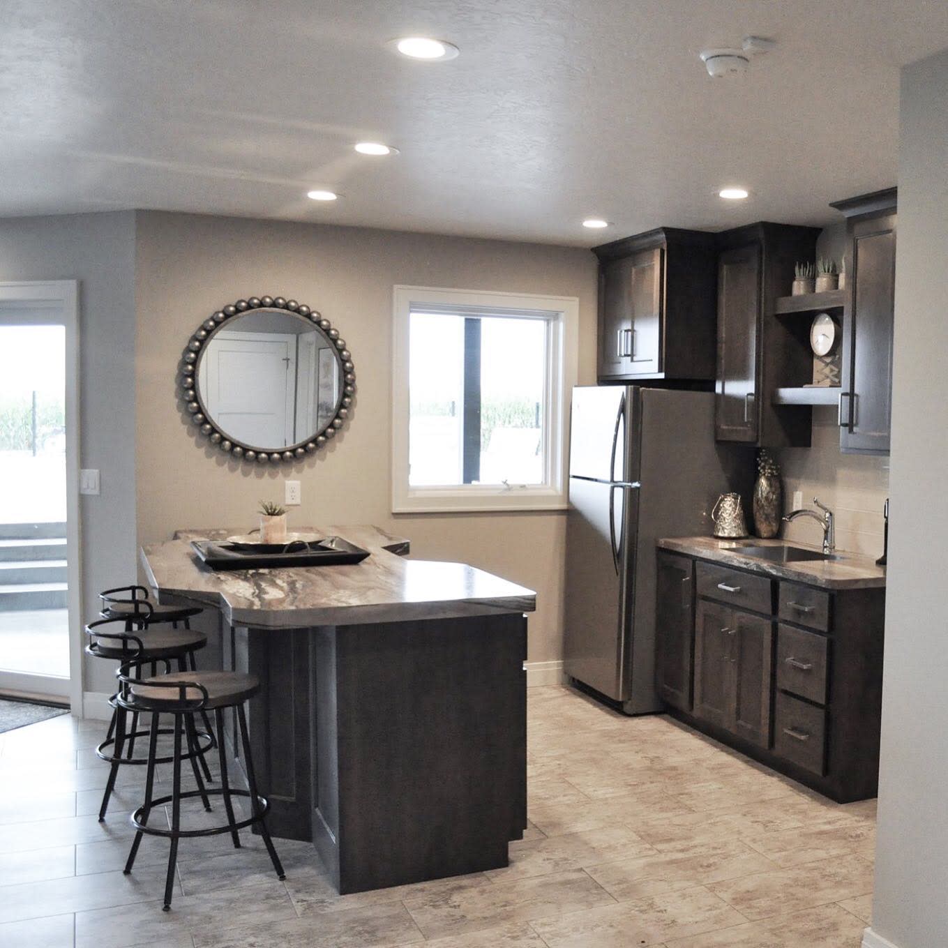 Modern kitchen with grey cabinets, marble countertops, and circular wall mirror.