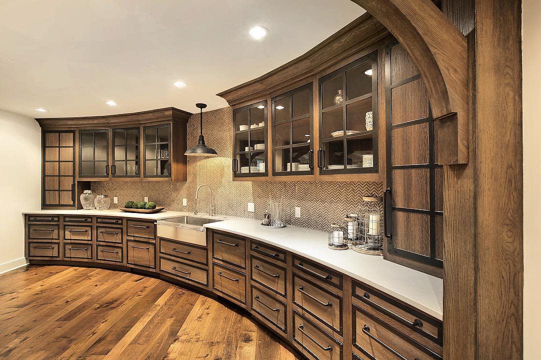 Large curved rustic kitchen with wood cabinets, farmhouse sink, and herringbone backsplash.