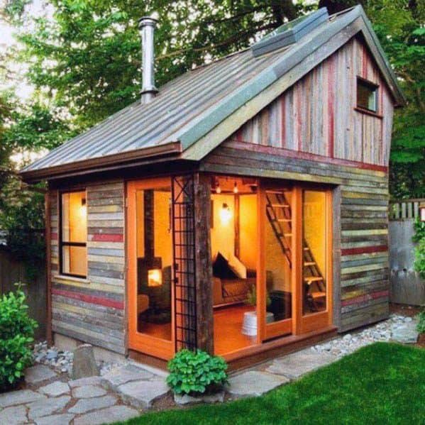 Rustic wood shed with metal roof, large windows, and cozy interior lighting.