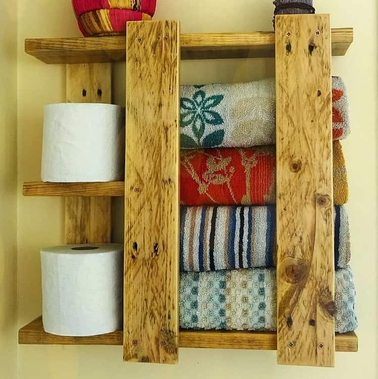 Rustic wooden pallet bathroom shelf holding towels and toilet paper rolls.