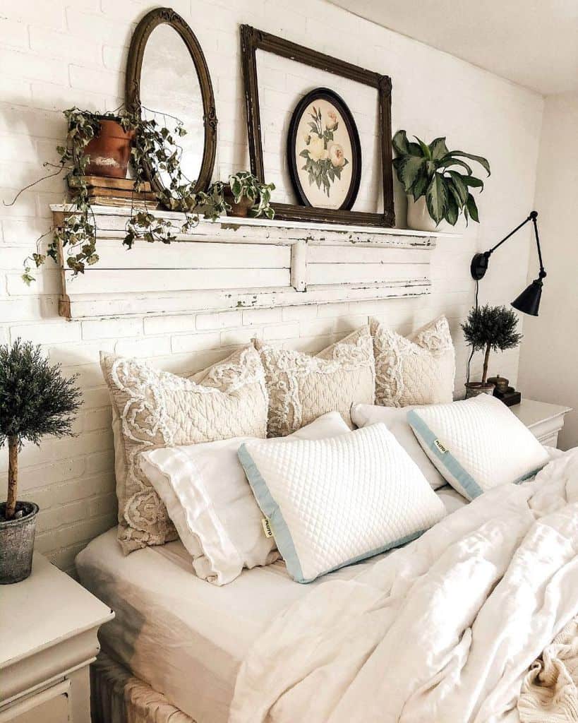 Cozy bedroom with pillows, plants, and decorative wall art on a shelf above a white brick wall