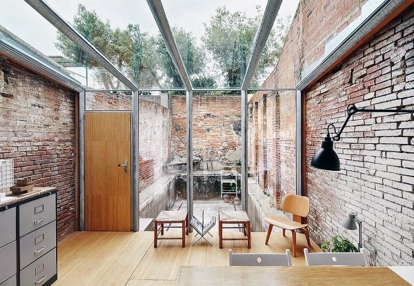 Sunroom with rustic brick walls, open glass ceiling, and minimalist seating for a modern industrial vibe.