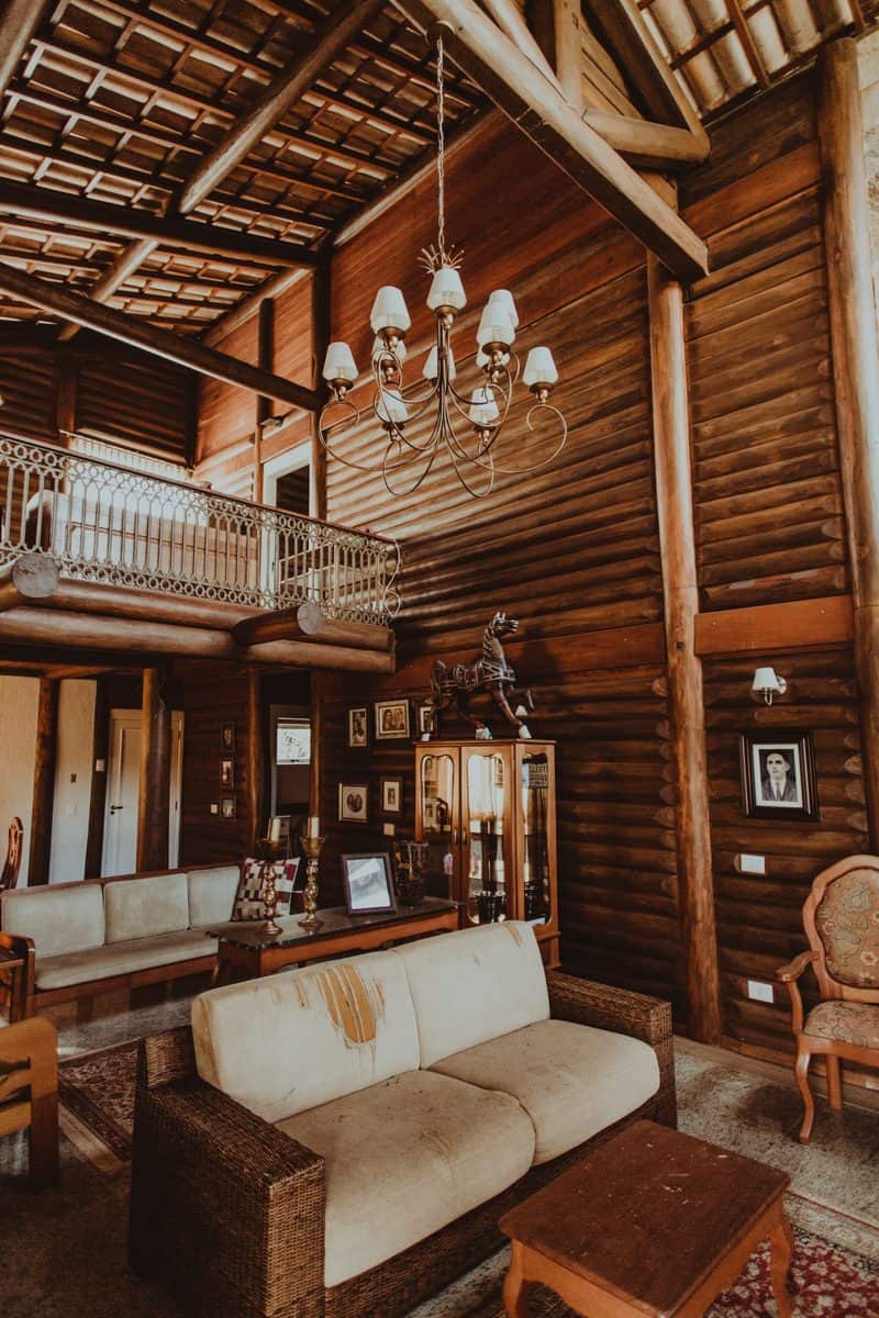 Rustic brown wooden living room with a chandelier, loft, and cozy seating area, featuring framed pictures on the walls