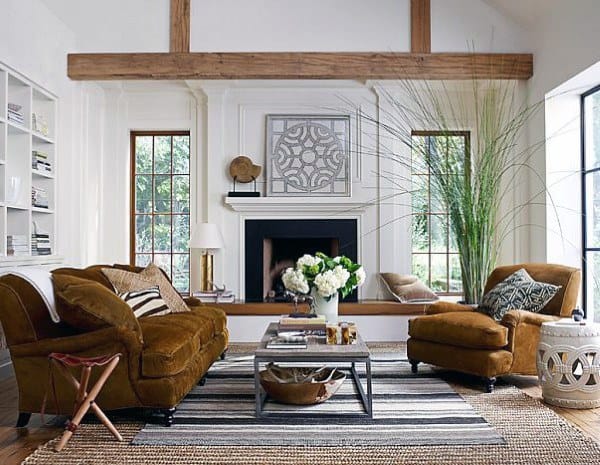 Cozy living room with brown sofas, a fireplace, large windows, plants, and a coffee table on striped and woven rugs