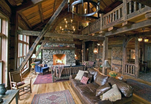 A spacious rustic living room with a stone fireplace, exposed wooden beams, comfortable seating, and an upper loft area, creating a warm and inviting atmosphere