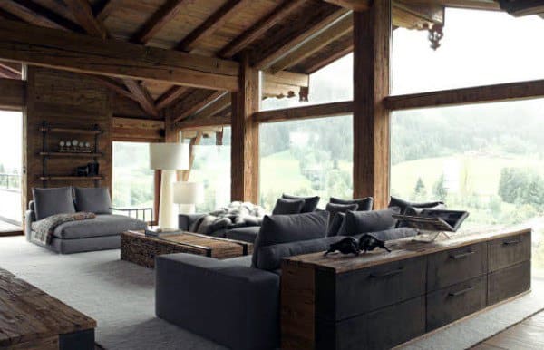 Cozy living room with wooden beams, large windows, gray sofas, and a scenic view of green hills outside