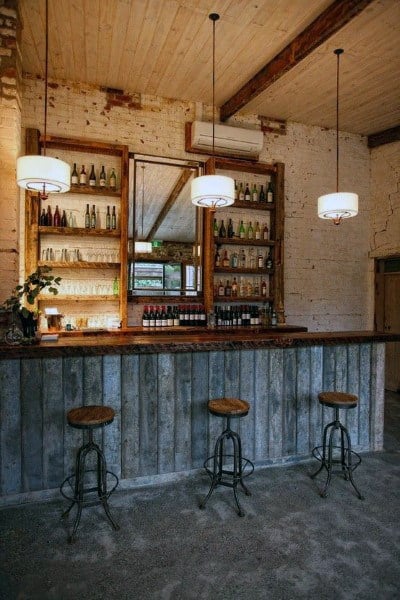 Rustic garage bar with wooden shelving, corrugated metal paneling, and industrial stools.