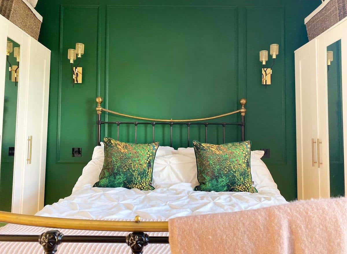 Cozy bedroom with a green accent wall, brass bed, and decorative pillows, flanked by white wardrobes and wall lamps