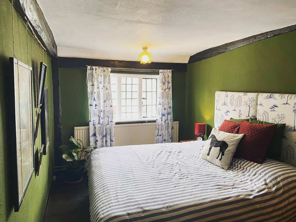 Cozy bedroom with green walls, striped bedspread, horse-themed pillows, and floral curtains by a window