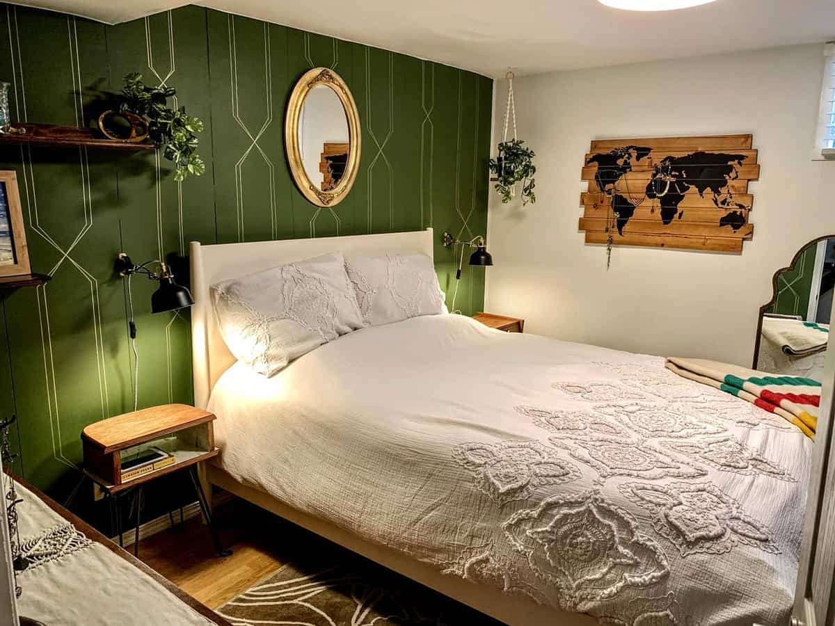 Cozy bedroom with a green accent wall, white bed, round mirror, and a world map decor piece