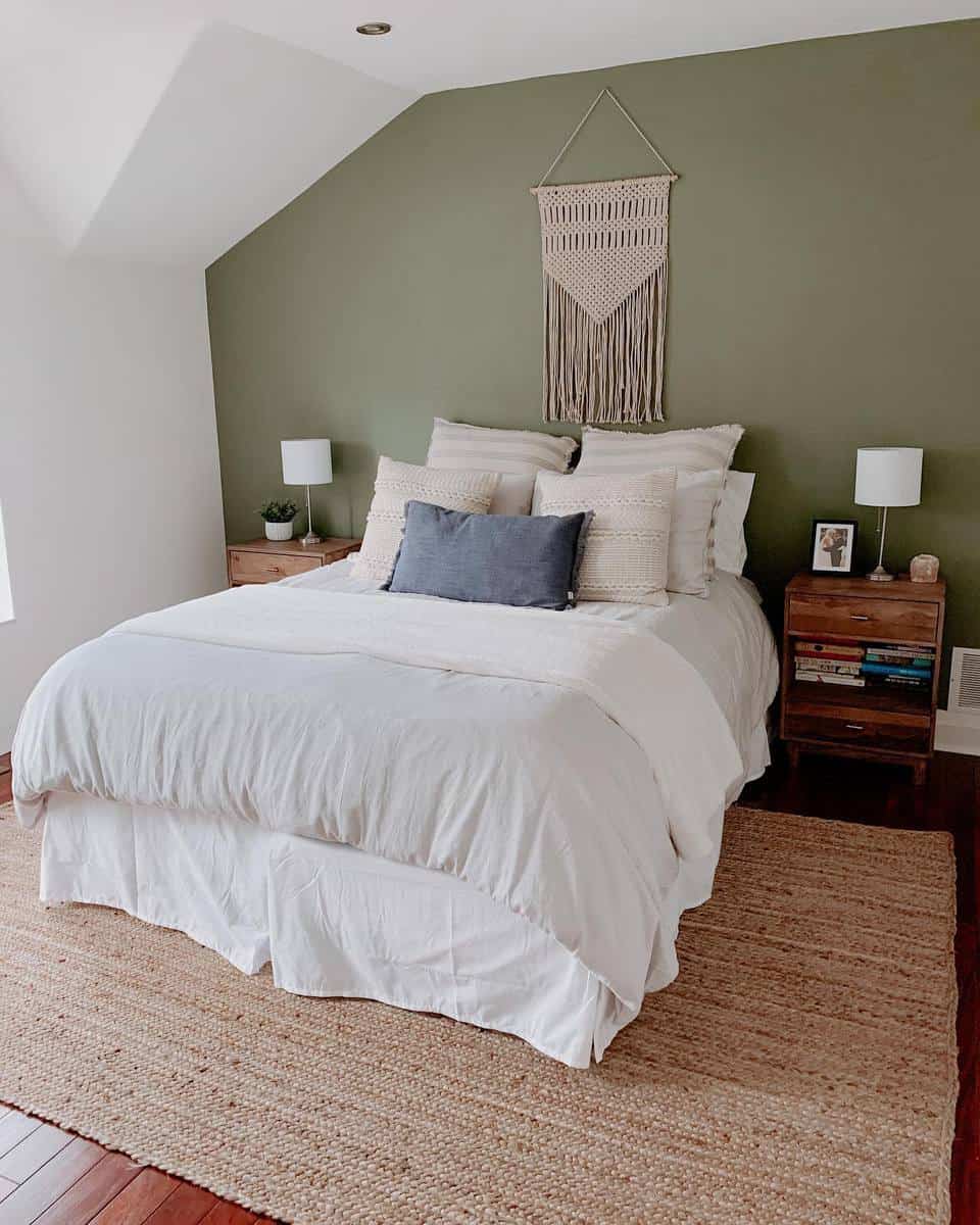 Cozy bedroom with a green accent wall, white bedding, pillows, wall hanging, bedside tables, and lamps