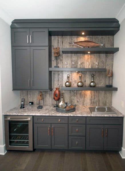 Rustic mini bar featuring grey cabinets, a natural wood backsplash, floating shelves with accent decor, a wine cooler, and a granite countertop.