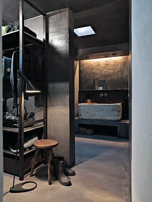 Industrial-style bathroom with concrete walls, a stone sink, and a metal shelving unit with clothing and boots