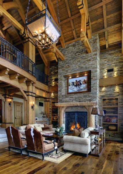 A rustic living room with a stone fireplace, vaulted wooden beams, elegant furnishings, and a large chandelier, creating a warm and inviting atmosphere with a touch of sophistication