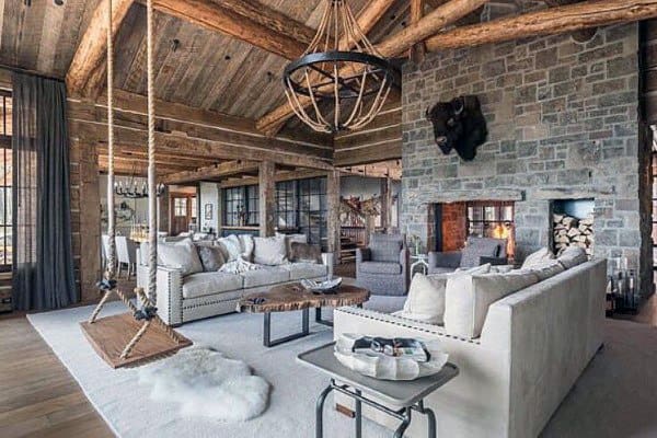 A rustic living room with exposed wooden beams, a stone fireplace, comfortable seating, and a unique swing chair, creating a cozy and playful atmosphere