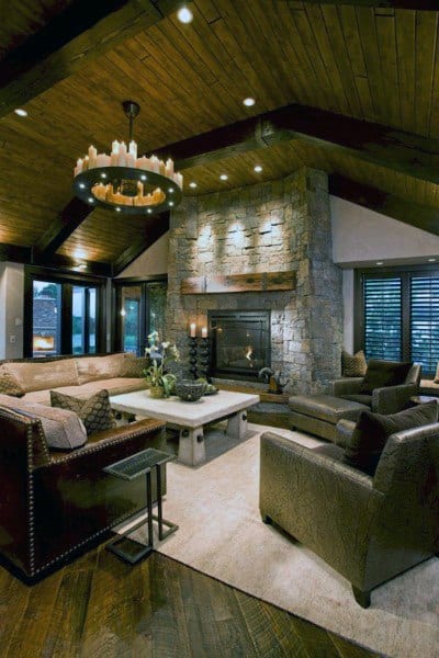 A rustic living room featuring a stone fireplace, exposed wooden beams, stylish lighting, and comfortable seating, creating a cozy and inviting space