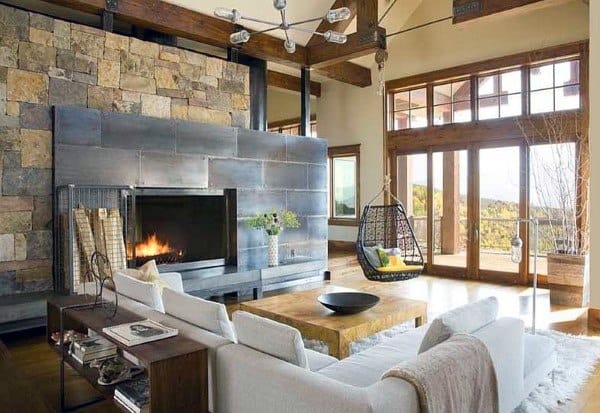 Modern living room with a stone fireplace, suspended chair, and large windows overlooking a scenic view