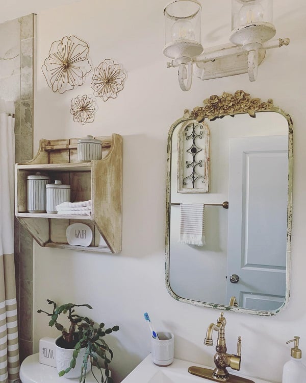 Cozy farmhouse bathroom with vintage decor, wooden shelves, a decorative mirror, and white accents