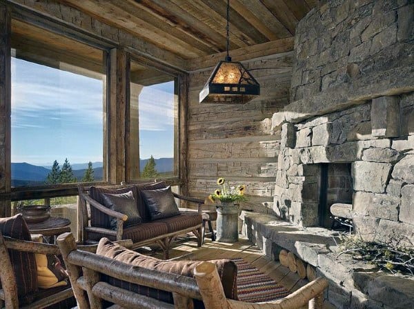 The rustic sunroom features a stone fireplace and wooden log furniture with cozy cushions.