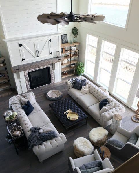 Cozy living room with large windows, white sofas, a black coffee table, and a fireplace beneath a ceiling fan