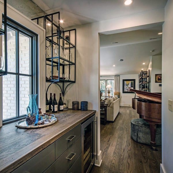 Rustic mini bar with vintage flair, featuring a wooden countertop, industrial-style shelving, a wine cooler, and cozy decor near a living space.