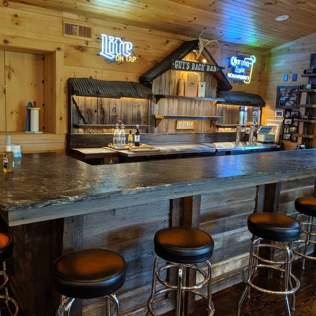 Rustic wet bar with reclaimed wood, corrugated metal accents, neon signs, and a stone countertop.