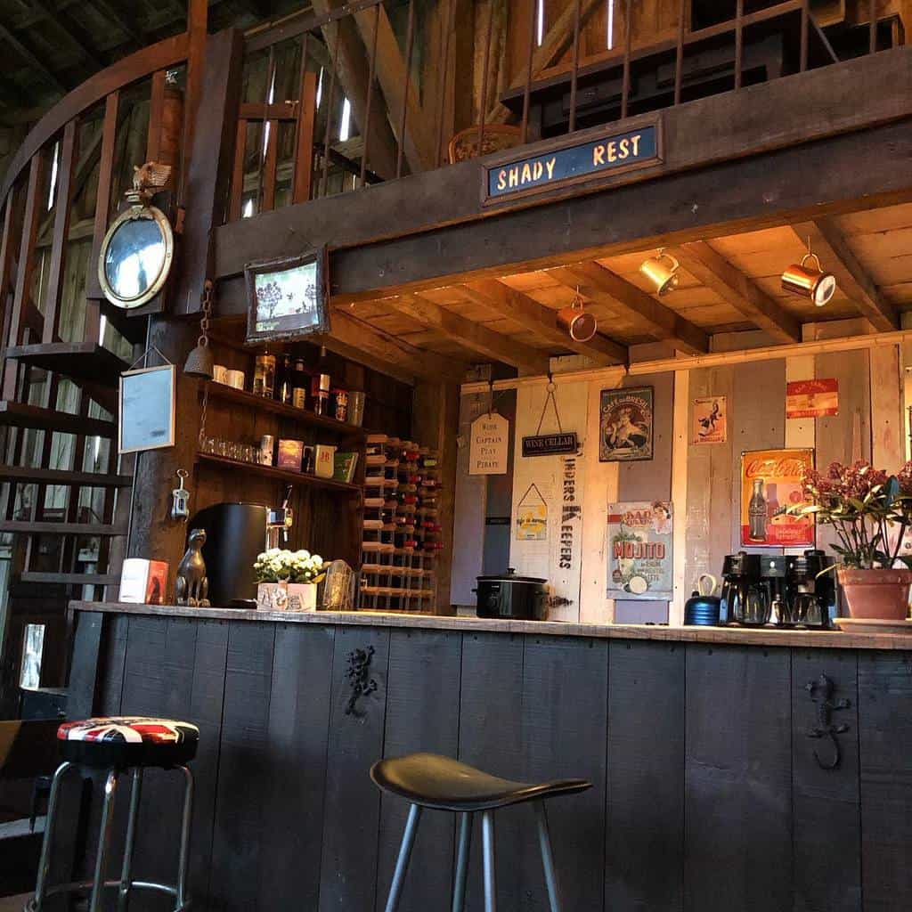 Rustic barn-style wet bar with vintage decor, wooden shelving, and cozy seating area.