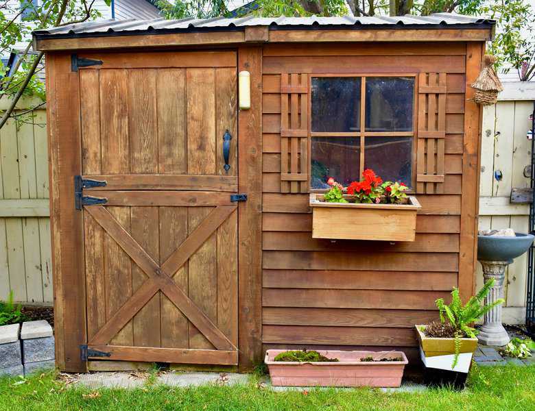 Rustic wood shed with barn-style door, window shutters, and flower box.