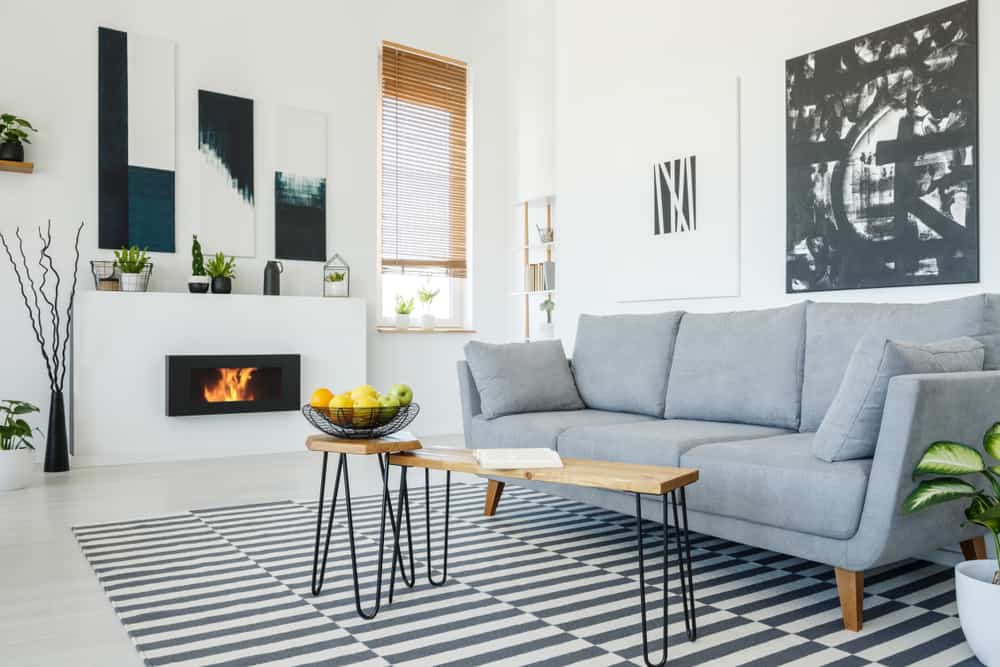 Bright Scandinavian living room featuring a gray sofa, striped rug, abstract wall art, modern fireplace, wooden table, and indoor plants