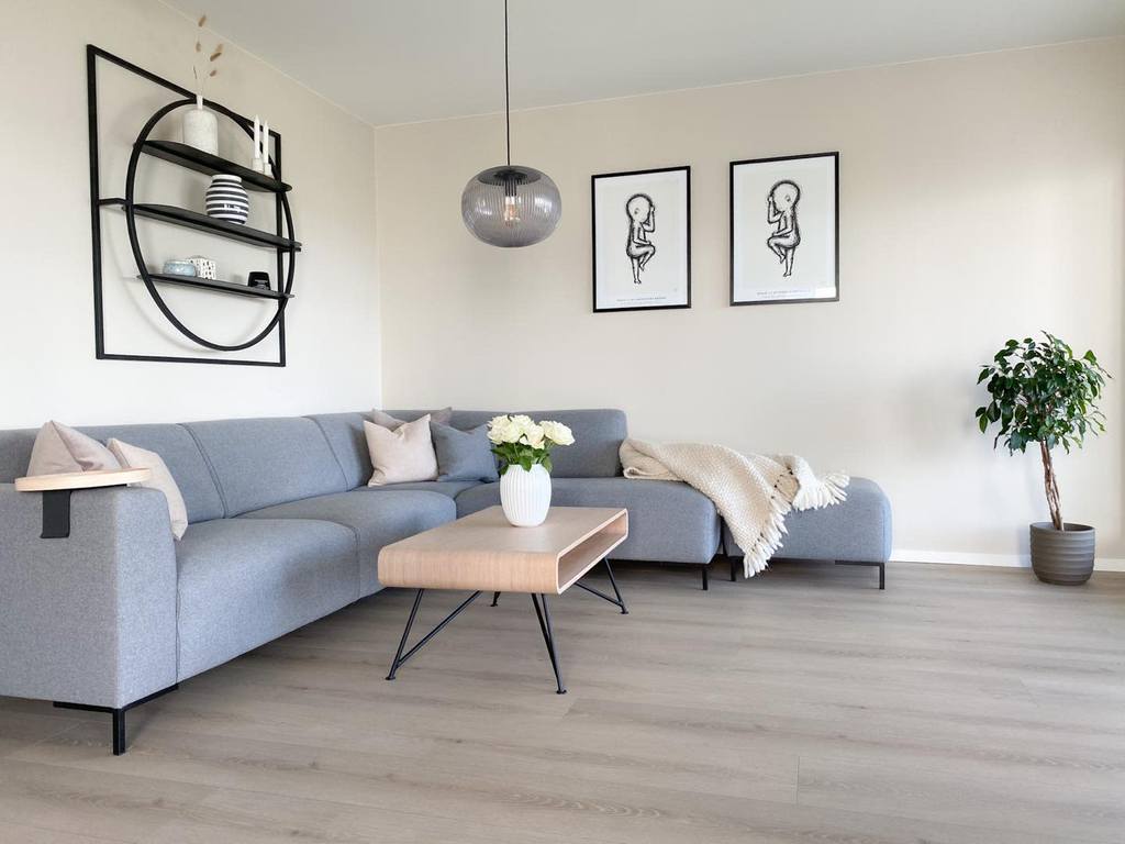 Scandinavian living room featuring a gray sectional sofa, light wood coffee table, round black wall shelf, and artistic wall decor