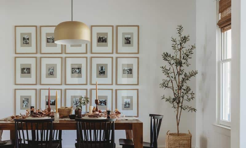 Elegant dining room with wooden table, black chairs, gold pendant light, and framed photo gallery.