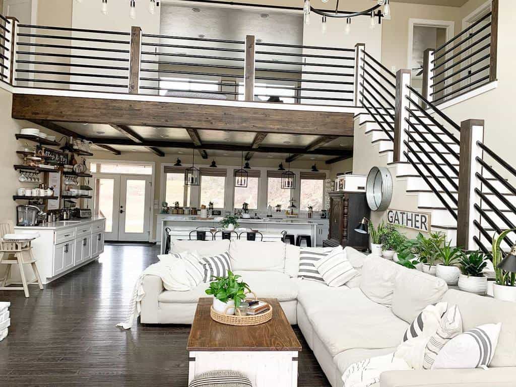 Spacious living area with white sectional sofa, wooden coffee table, open kitchen, loft, and indoor plants