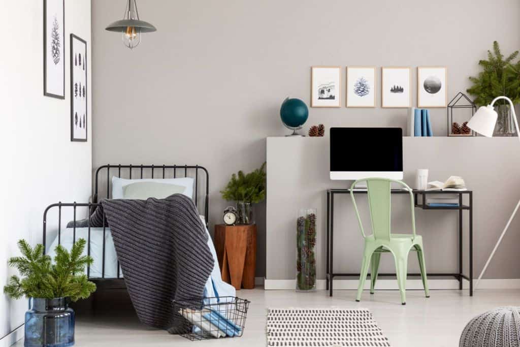 Modern bedroom with single metal bed, black desk, and green metal chair.