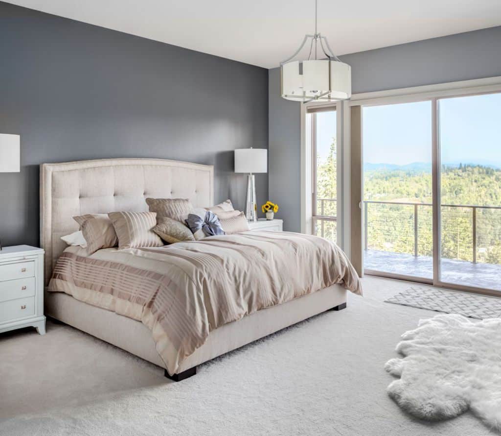 Modest master bedroom with tufted bed, white rug, and balcony with forest view.