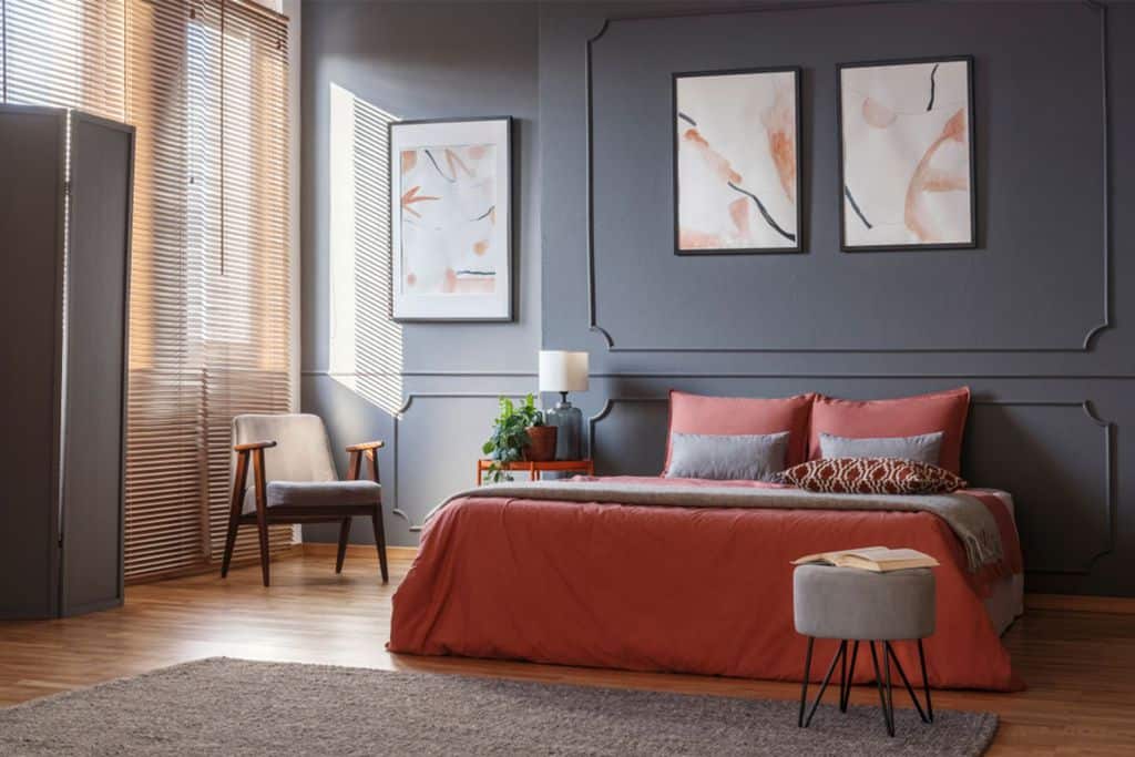 Gray bedroom with red bedding, abstract wall art, and wooden blinds.