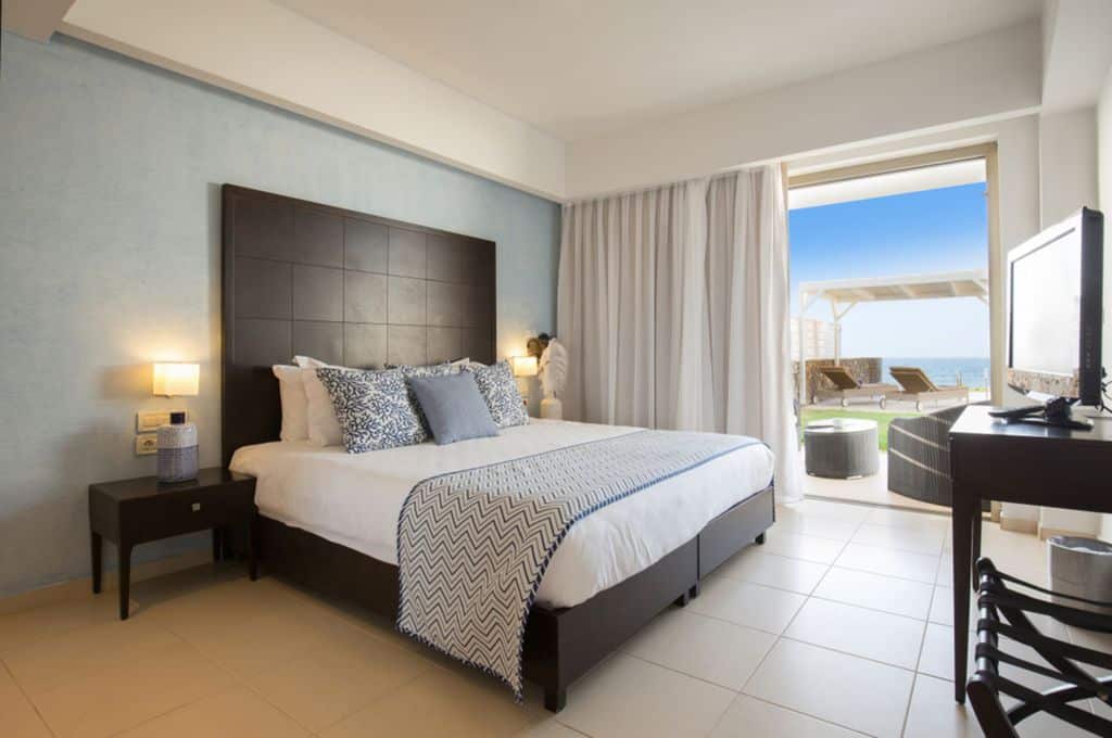 Modern bedroom with tile floor, large bed, and open patio with ocean view.