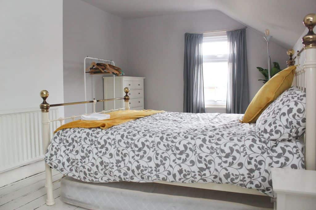 Elegant bedroom with four-poster bed, patterned bedding, and small clothes rack.