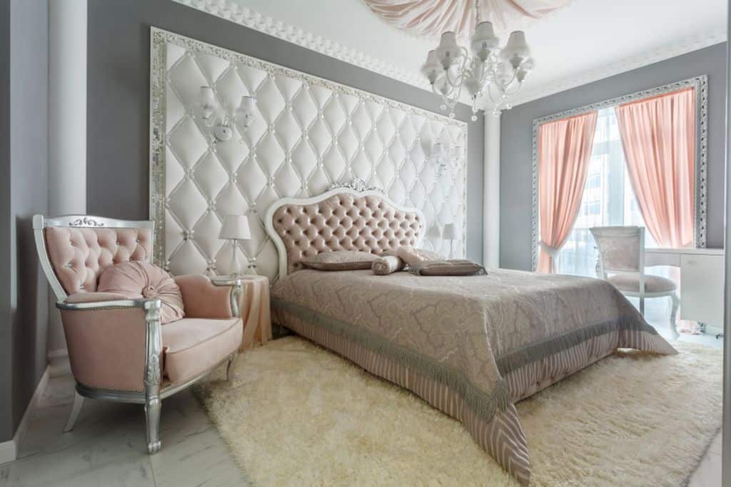 Elegant bedroom with tufted headboard, pink accents, chandelier, and plush rug.