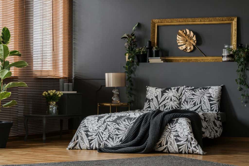 Luxury bedroom with dark walls, gold frame wall art, and leafy bedding pattern.