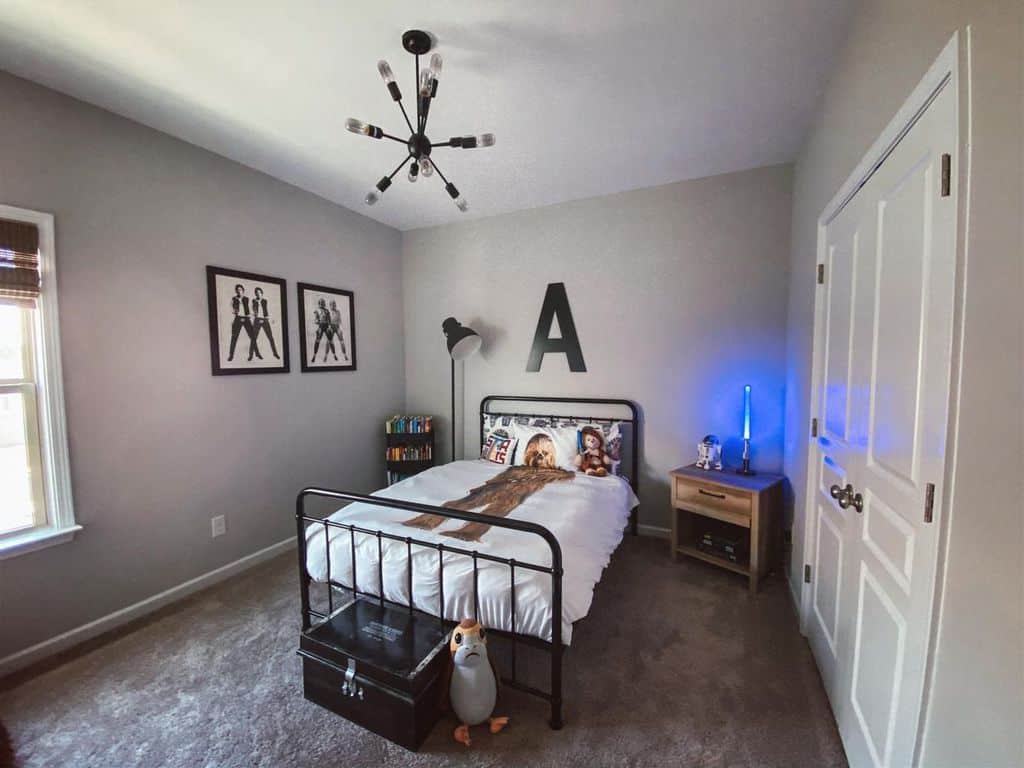 Small kids bedroom with black metal bed, Star Wars decor, and wall art.